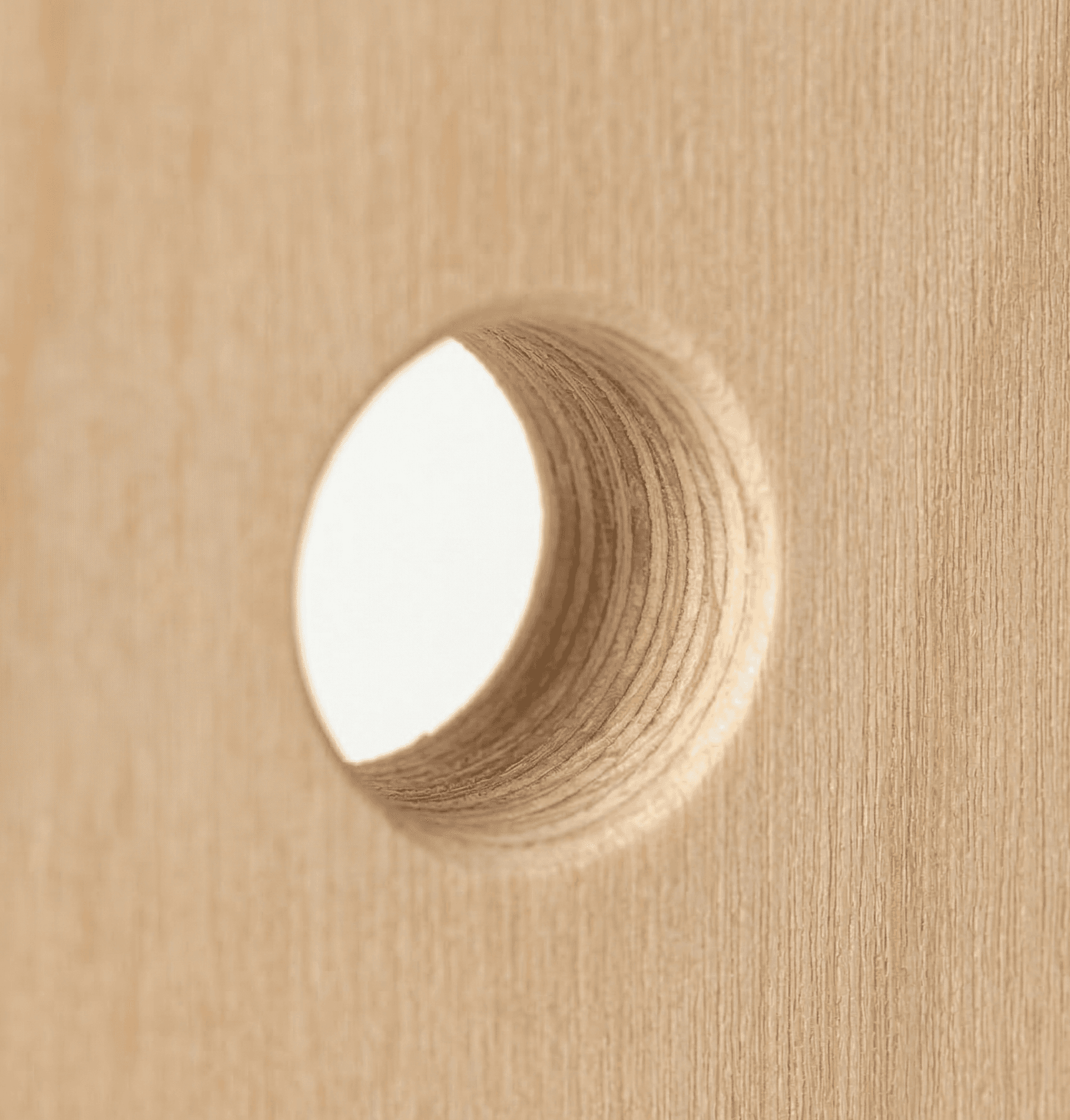 Close-up of CNC-drilled hole showing birch plywood layers